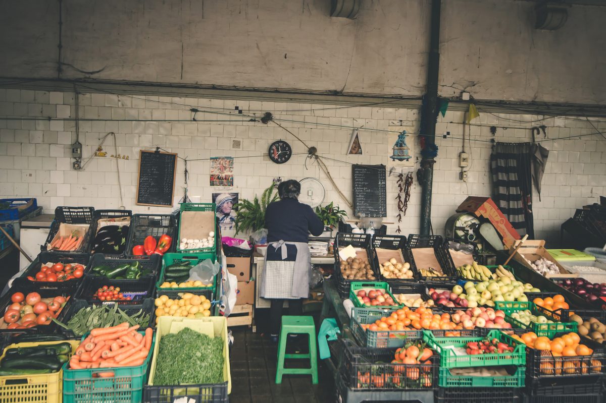 An elderly merchant selling fresh fruits and vegetables at Mercado do Bolhão, an outdoor market in Porto
