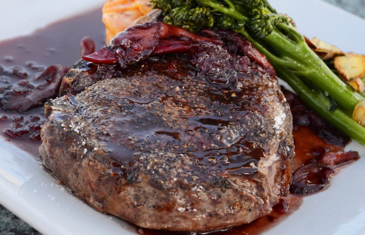 Beef and broth on a white plate with vegetable at the side