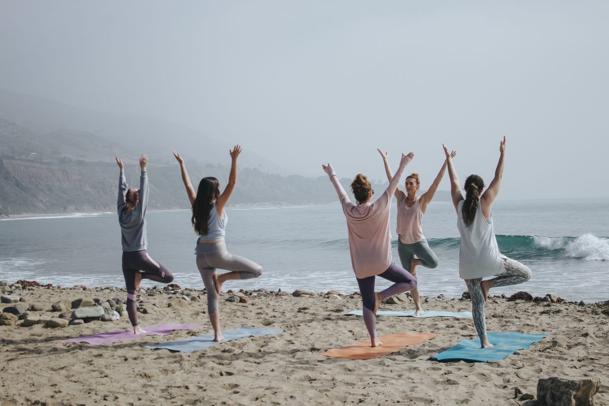 group of women practicing yoga on a beach