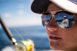 Woman wearing Costa sunglasses with another woman fishing reflected in the lens.