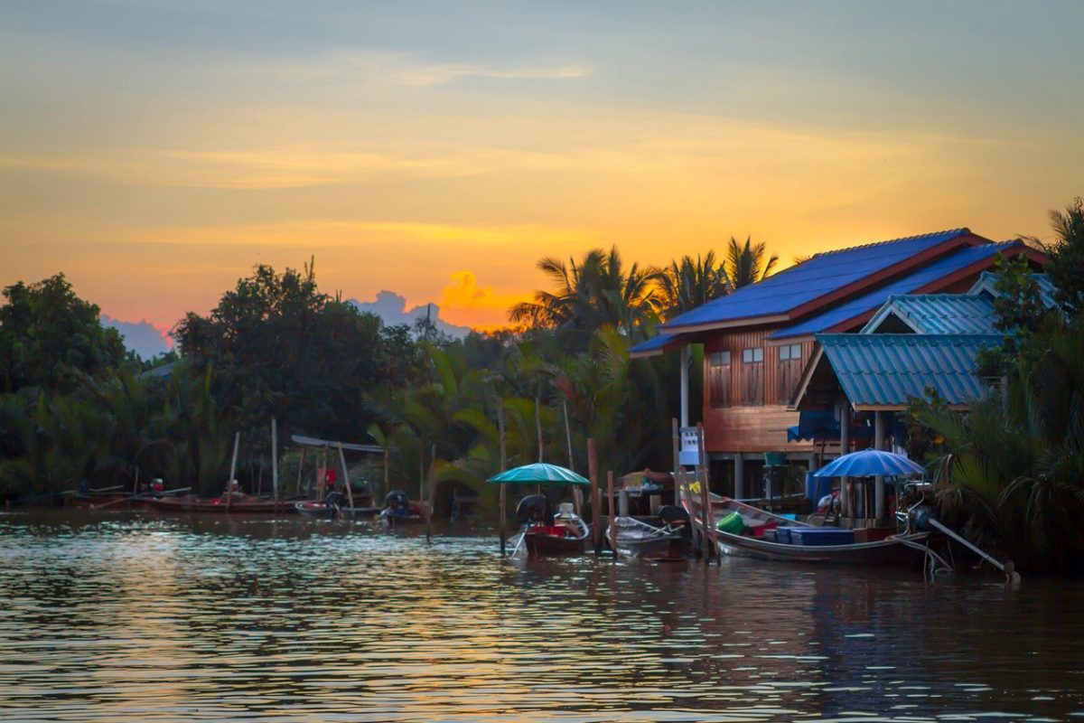 Stilt houses and floating market boats on a river at sunset