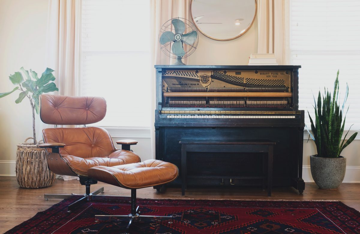 Chair, grand piano. plants and a mirror hanging on the wall