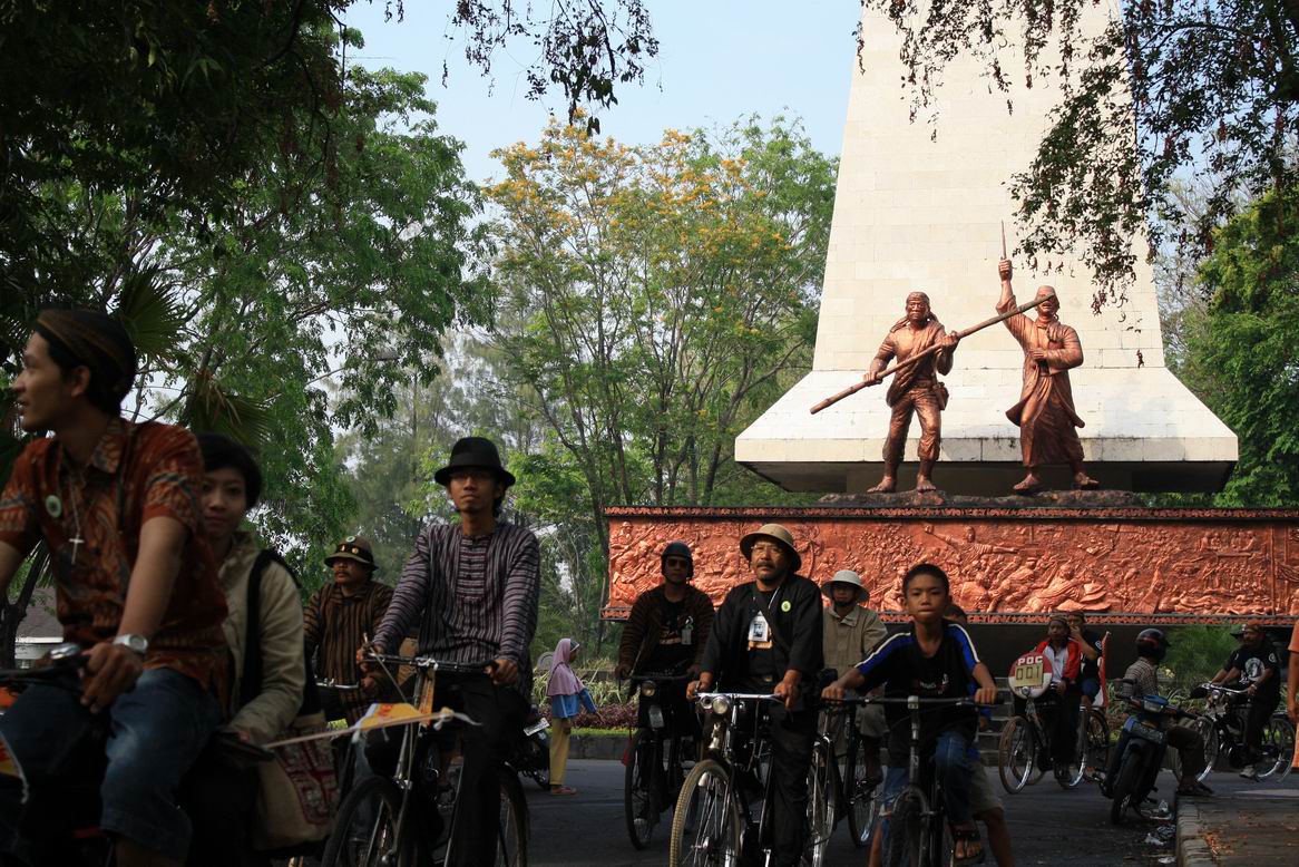 Men and kids cycling on a bicycle near the Surakarta Monument, Indonesia
