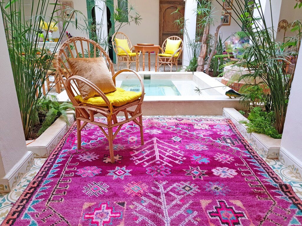 Wooden chair on a pink handwoven rug in a courtyard of a riad, one of the best things to do in Morocco is to stay in colorful traditional riads
