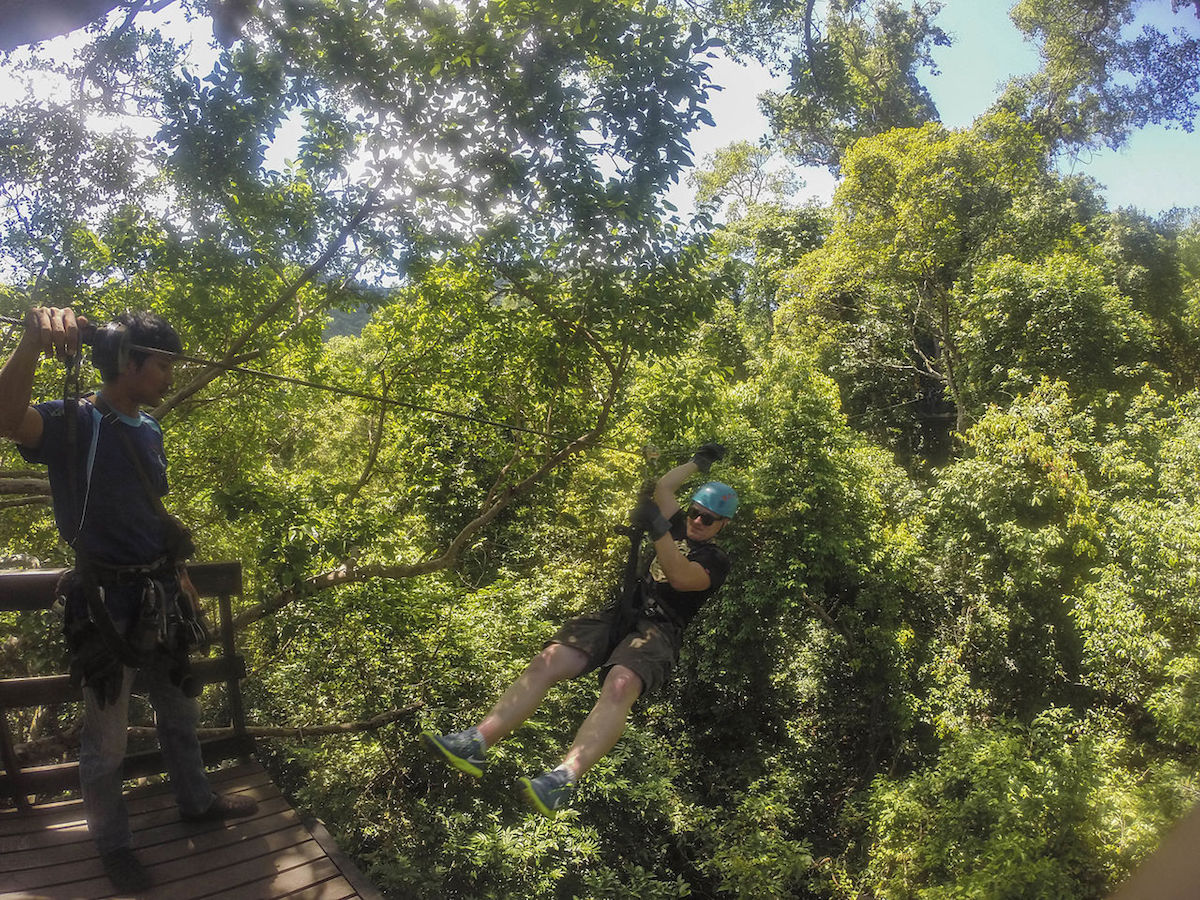 a man preparing to zipline down into the forest