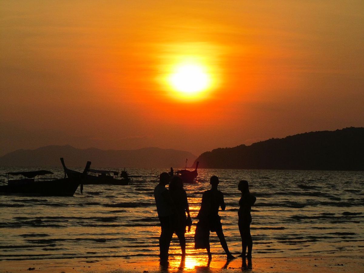 four people enjoying the view of the sunset on the beach shore