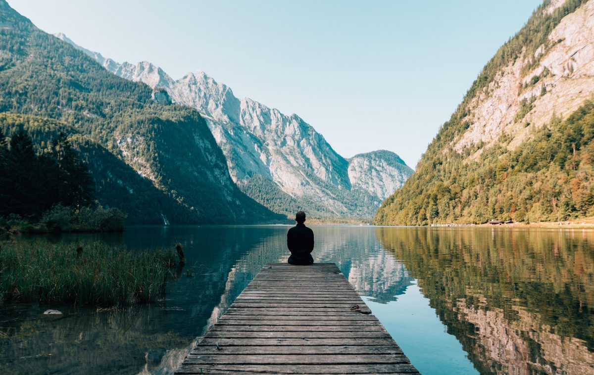 Man enjoying the view A man sitting at the pier of a lake with mountains in the near distance
