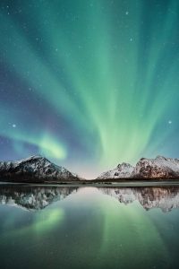 Yellow green aurora lights over mountains and a calm body of water with many stars at night