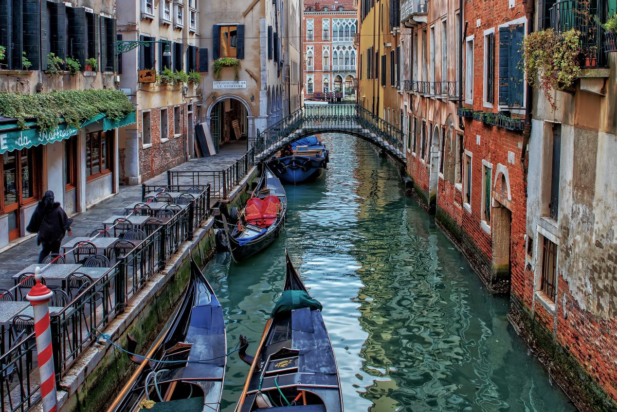 A small street in Venice with a canal and boats and a bridge