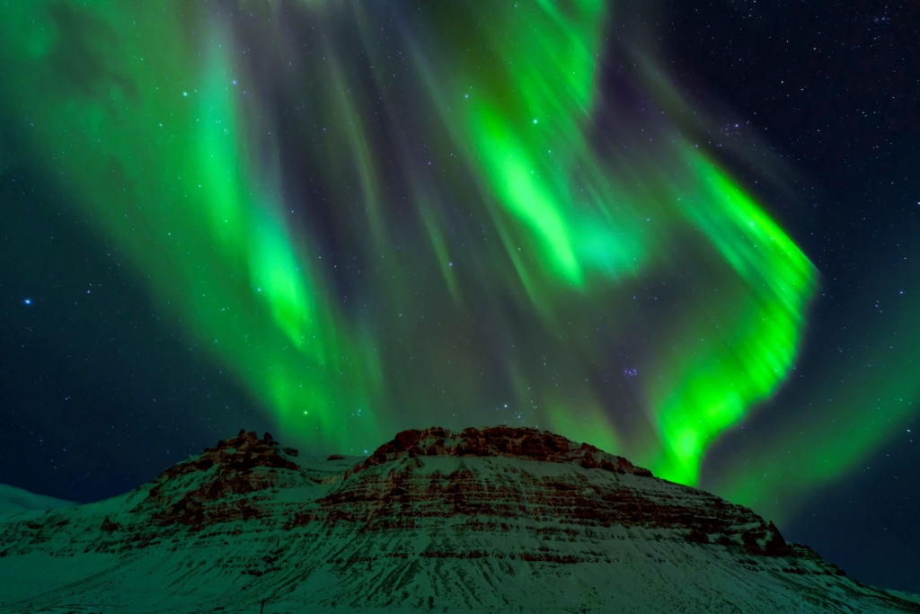 The exploding northern lights are waving around in the night sky, on top of snowy mountain in Michigan.