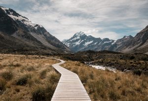 A walkway stretches across grasslands with a mountain range seen at a distance in the Hooker Valley Track, Mount Cook National Park, New Zealand