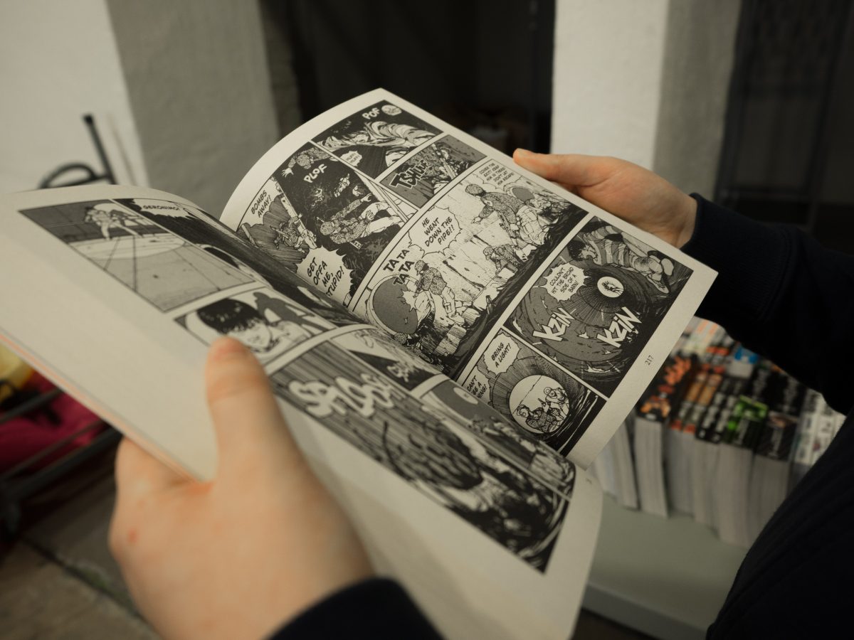 Closeup of hands holding open a manga that’s black and white with other mangas in the background