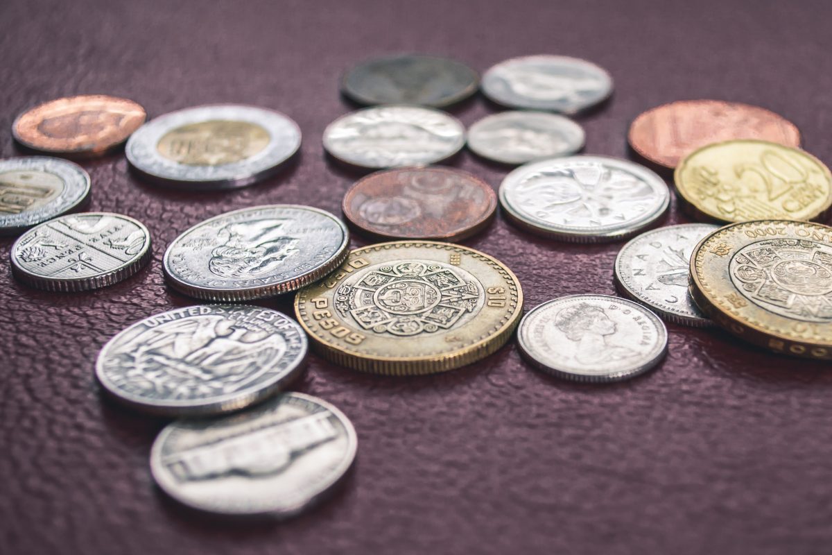 Photo of coins of different weights, colors, and currencies laid out on a brown leather surface