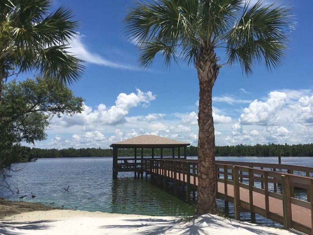 Swaying palm trees on white sand with a backdrop of a wooden pier at Cypress Cove Nudist Resort