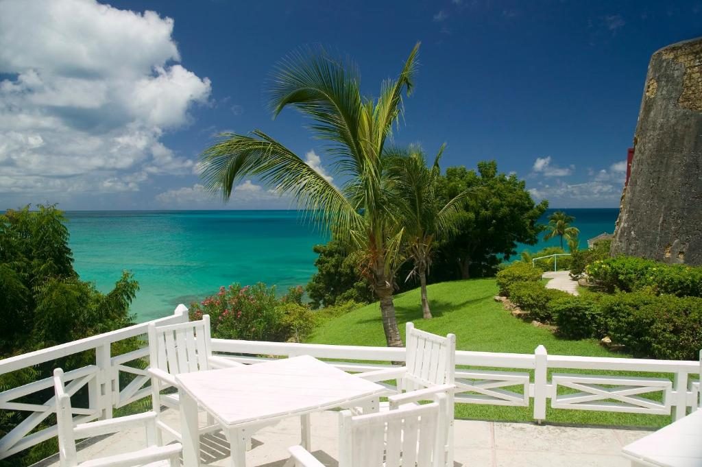 White chairs and table framed by white fence facing the Caribbean ocean at Hawksbill by Rex Resorts  