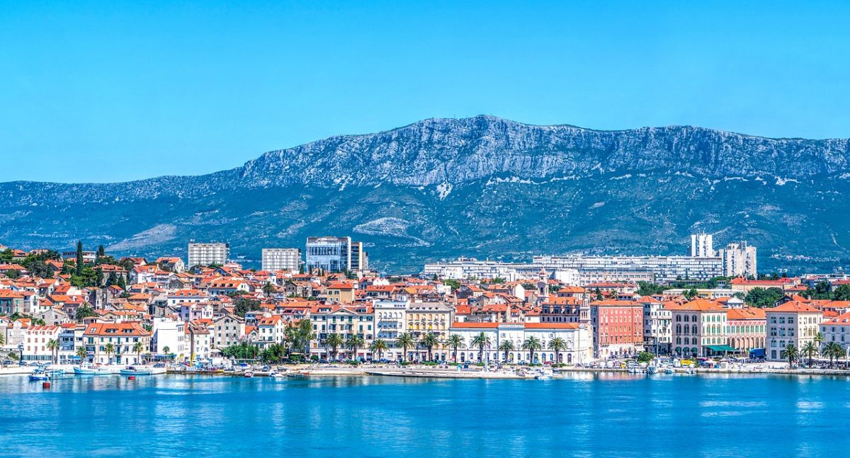 Various buildings line the shore as a mountain range stands in the background in Split, Croatia