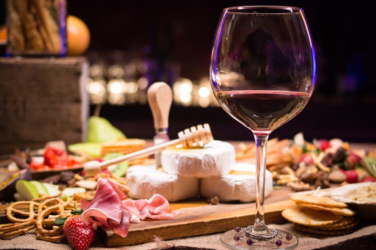 Red wine and a platter of cheeses spread over the table. 