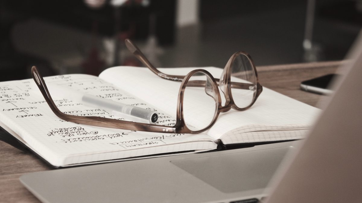 brown glasses, black pen,  and journal on top of laptop