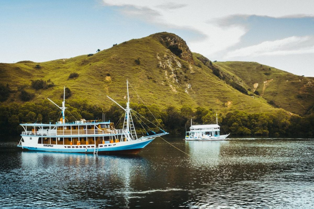 photo of a sailing boat near the green hills photo of a sailing boat near the green hills