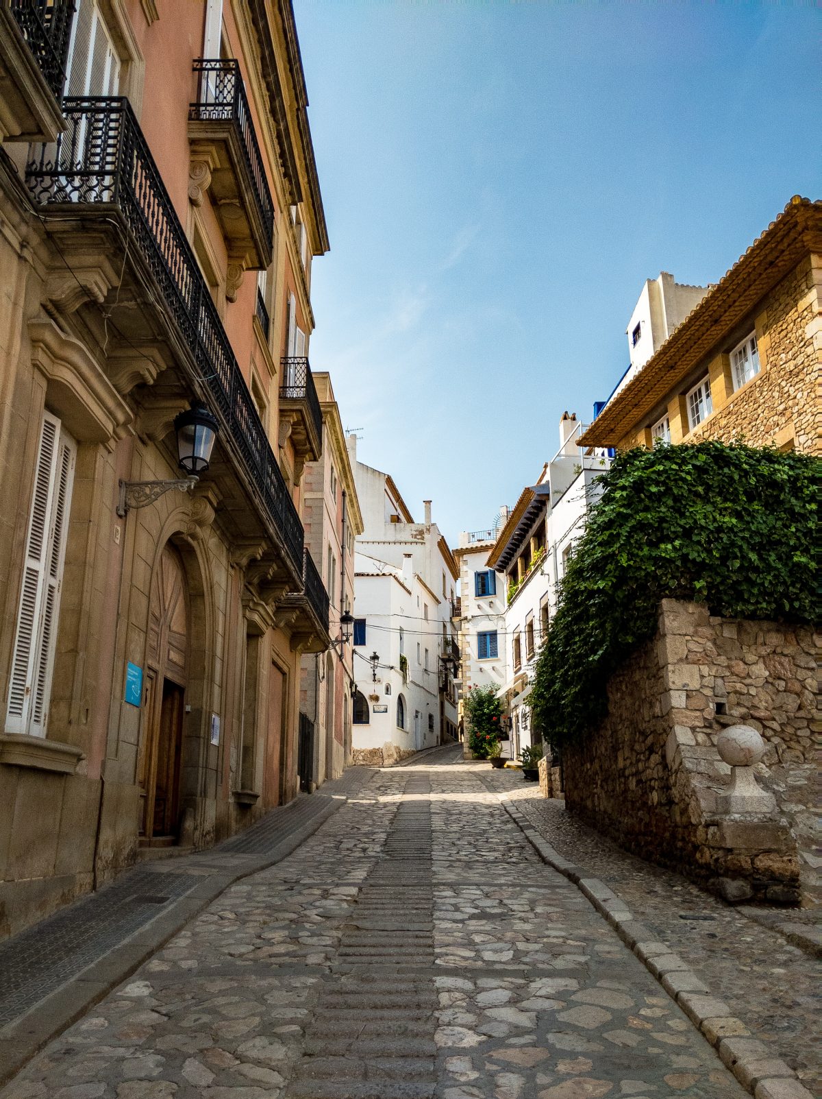 Sitges, Spain White and brown buildings line either side of a stone street in Sitges, Spain