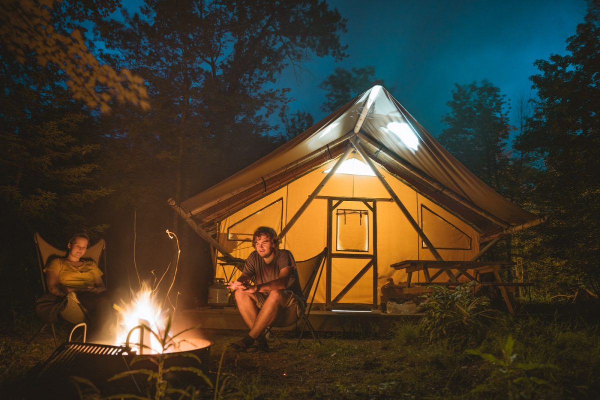 Camper cooking s'mores on a campfire in front of glamping tent