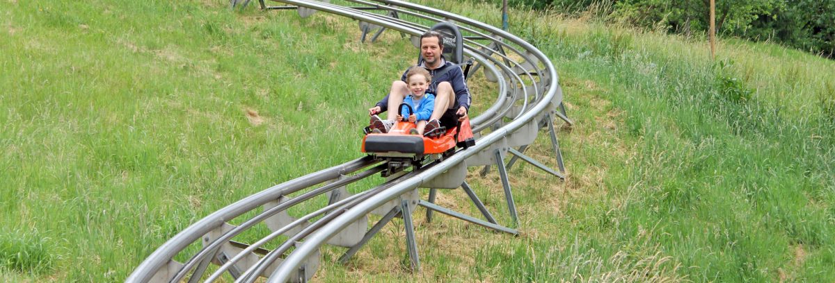  a man and a child happily riding the toboggan in black forest