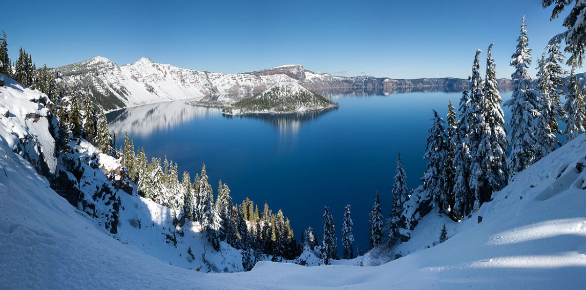 a crater lake surrounded by snow-capped mountains and pine trees