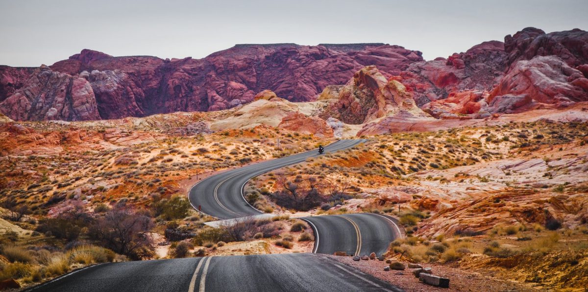 a motorcycle traversing the road towards the massive red rocks 