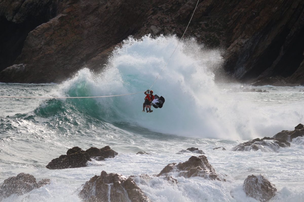 two people bravely ziplining above the crashing waves