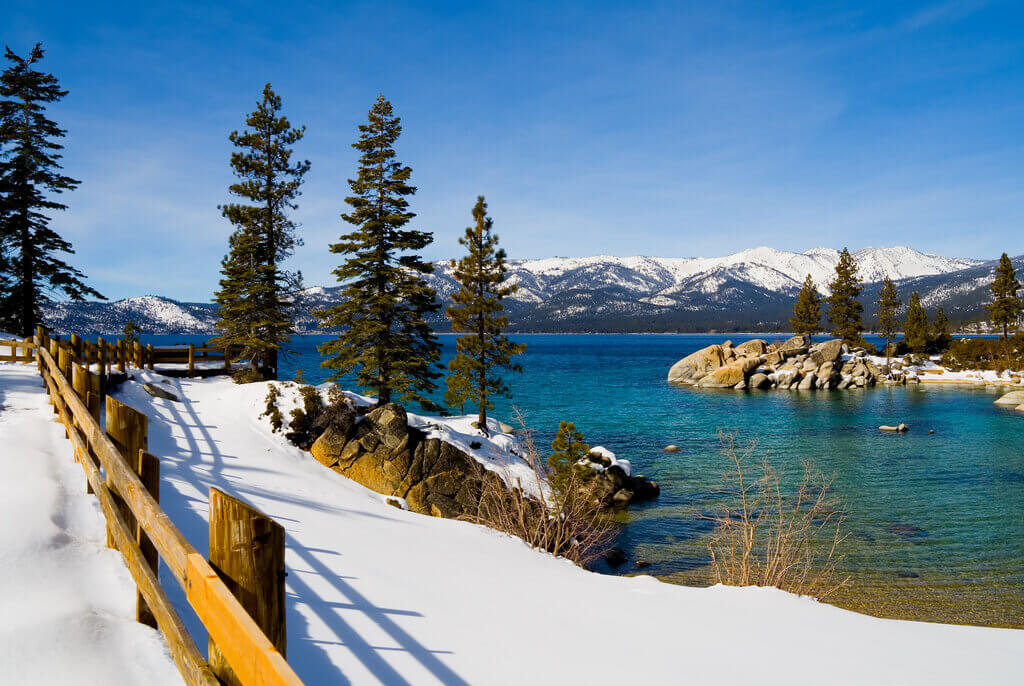 Snowy path next to the emerald lake with a view of snow capped mountains at Lake Tahoe