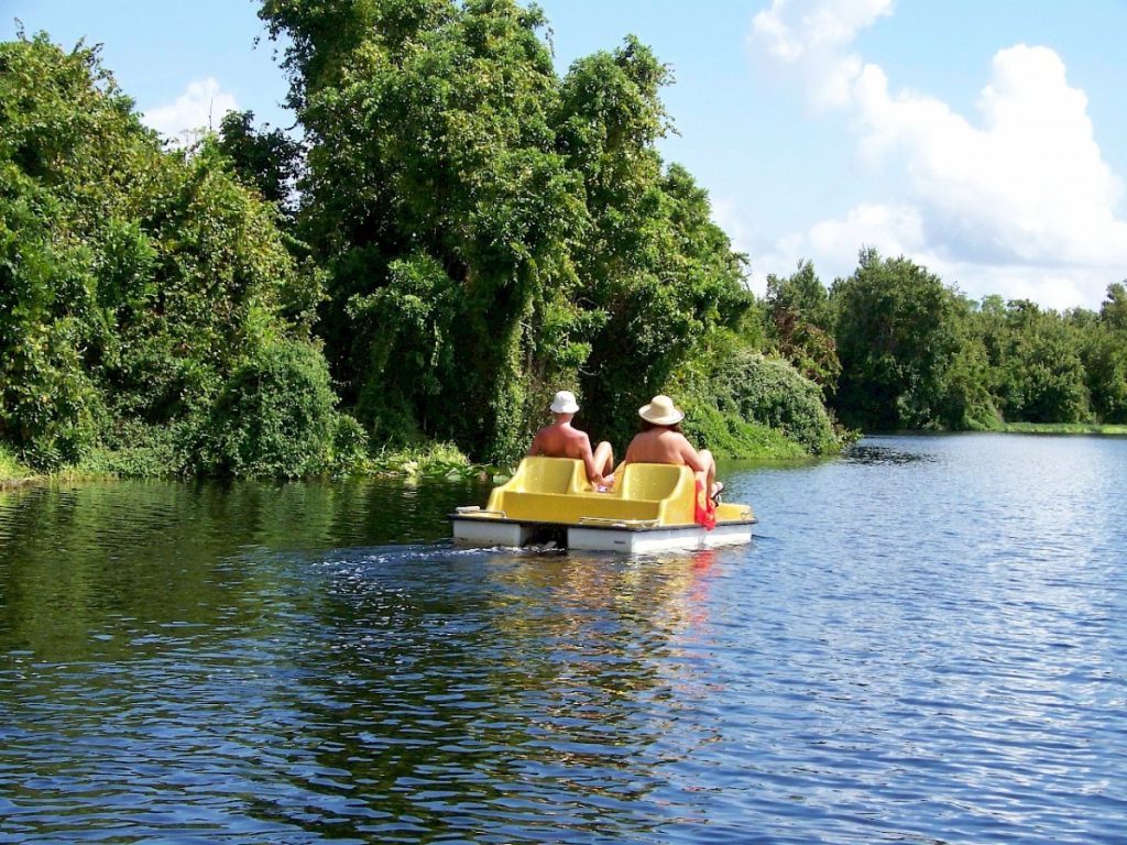 Two naked people wearing hats pedaling on a paddle boat.