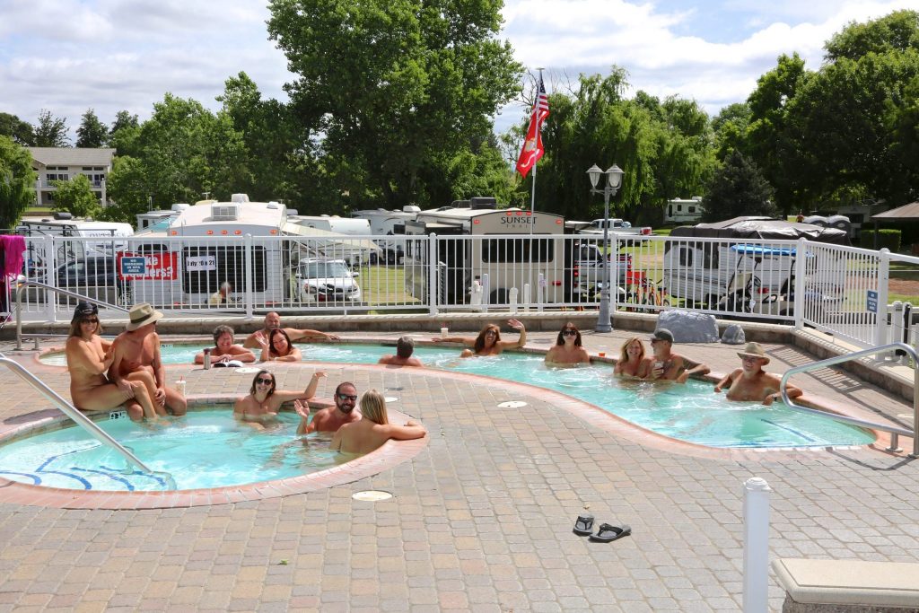 Nude people lounging and swimming in an outdoor pool.