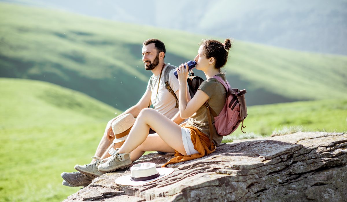 Couple traveling in the mountains Couple sitting on a rock in the mountains, while woman drinks from a collapsible water bottle.