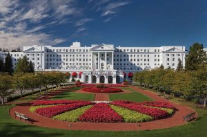 Front view of The Greenbrier Resort with landscaped yard and lush trees.