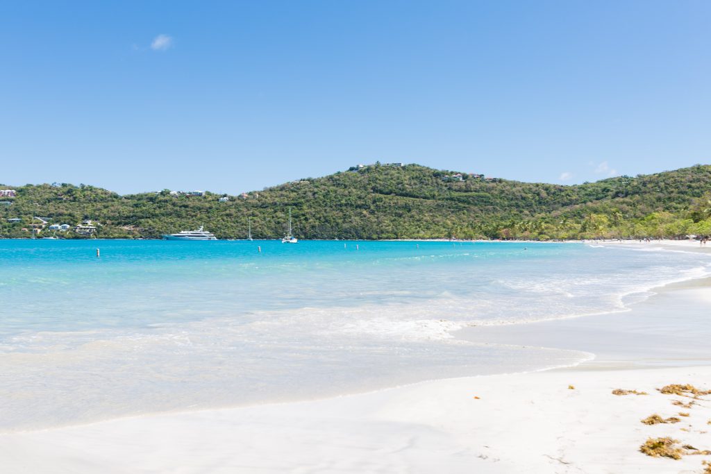 Boats on the waters of Magens Bay Beach in St. Thomas against a backdrop of rolling hills and palm trees.