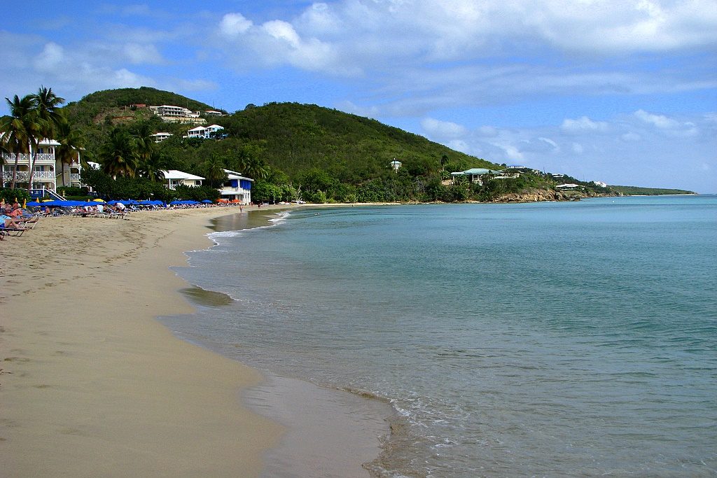 Row of people lounging under blue umbrellas along the shores of Morningstar Beach in St. Thomas.