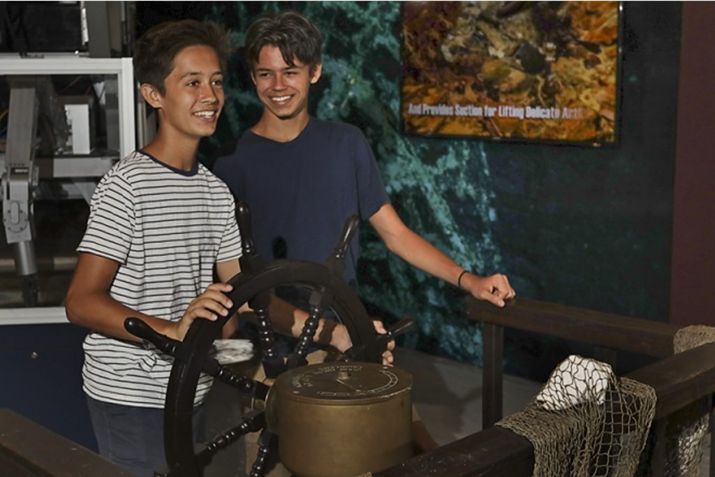 Two young boys smiling while behind a steering wheel at the Pirate Treasure Museum, St Thomas.