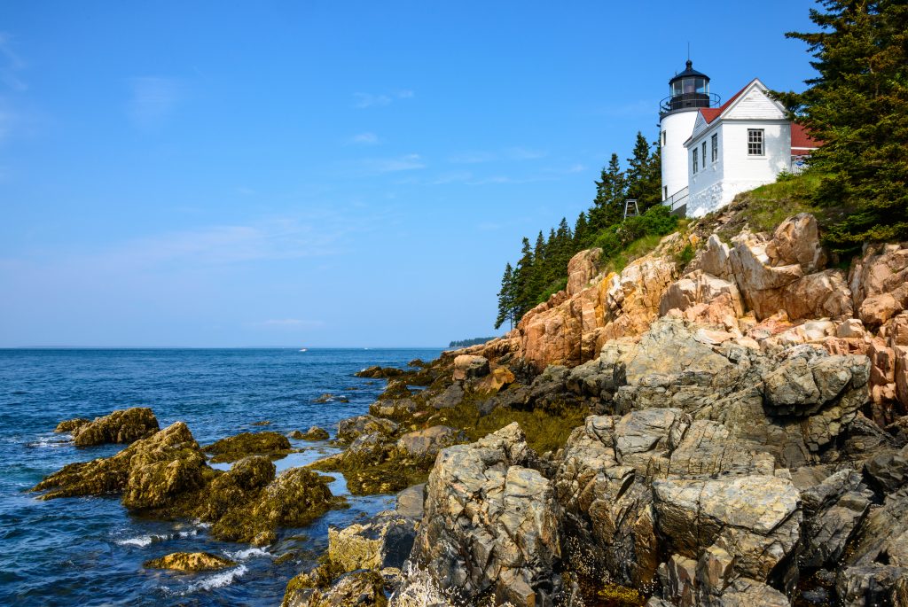 Rocky shores near the water with a lighthouse and trees at Acadia National Park, Maine.