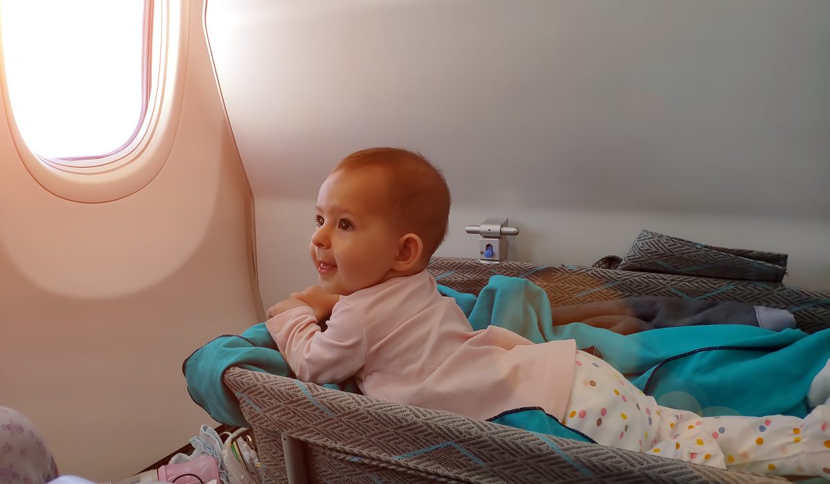 Smiling child lounging on a travel bassinet on an airplane.