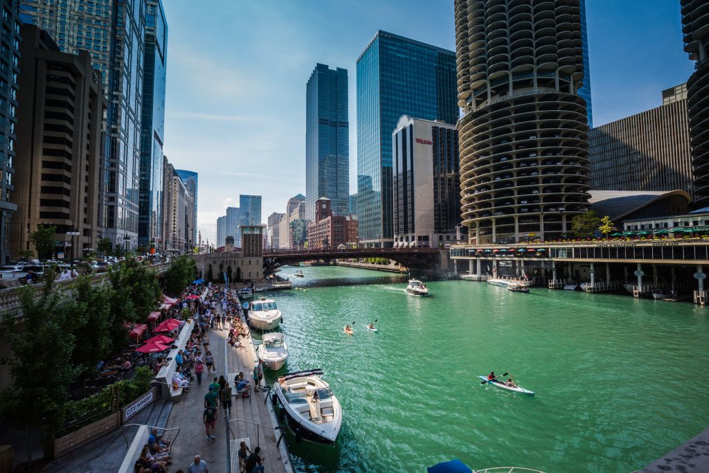 Chicago Riverwalk, with boats docked riverside and people kayaking in the water. 