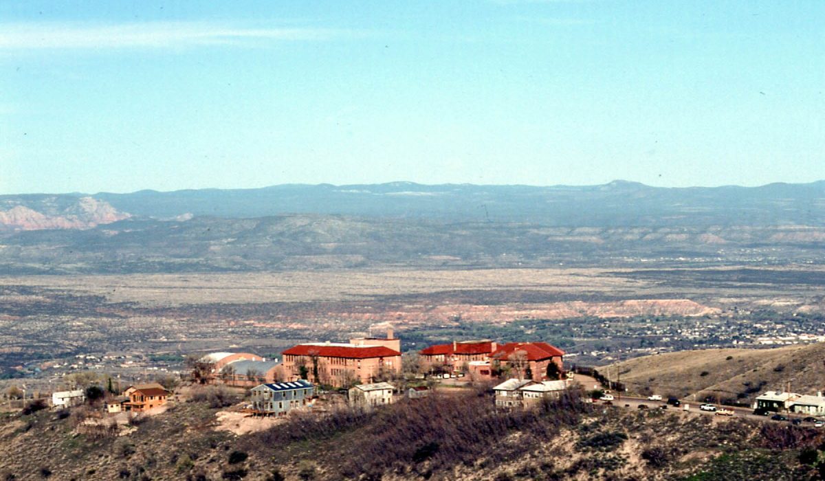 Wide shot photo of Jerome, one of the ghost towns in Arizona, surrounded by plateau and with mountain ranges in the background.