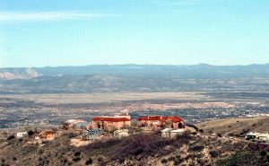 Wide shot photo of Jerome, one of the ghost towns in Arizona, surrounded by plateau and with mountain ranges in the background.