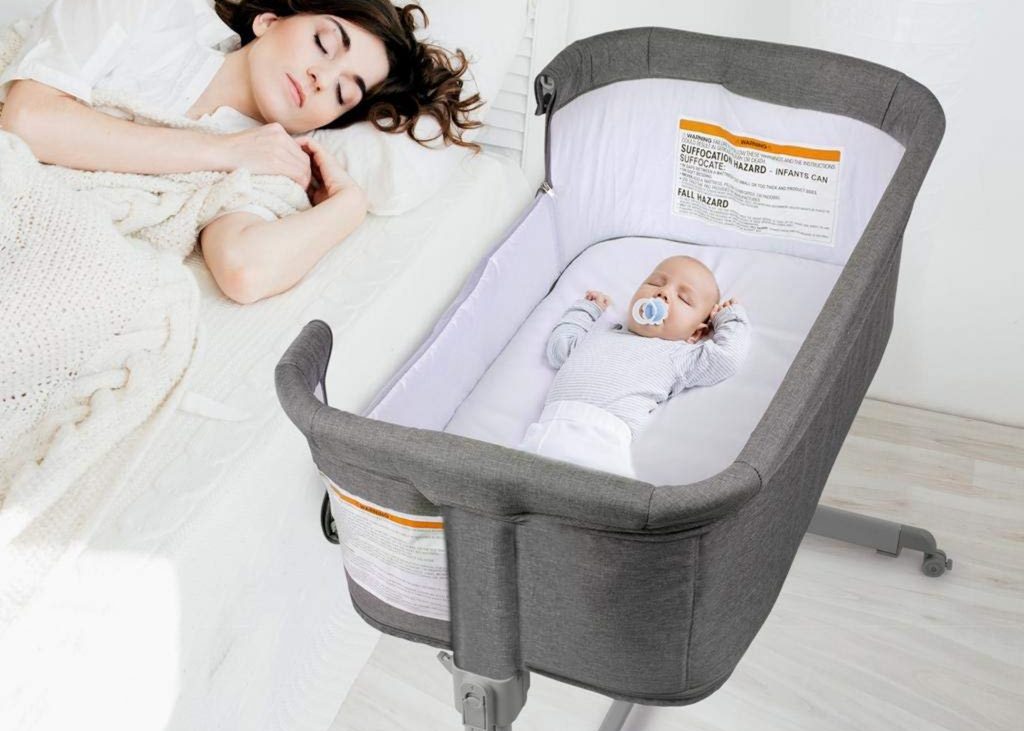 Baby sleeping soundly in the KoolerThings 3-in-1 Folding Portable Crib next to their sleeping mother on a bed.