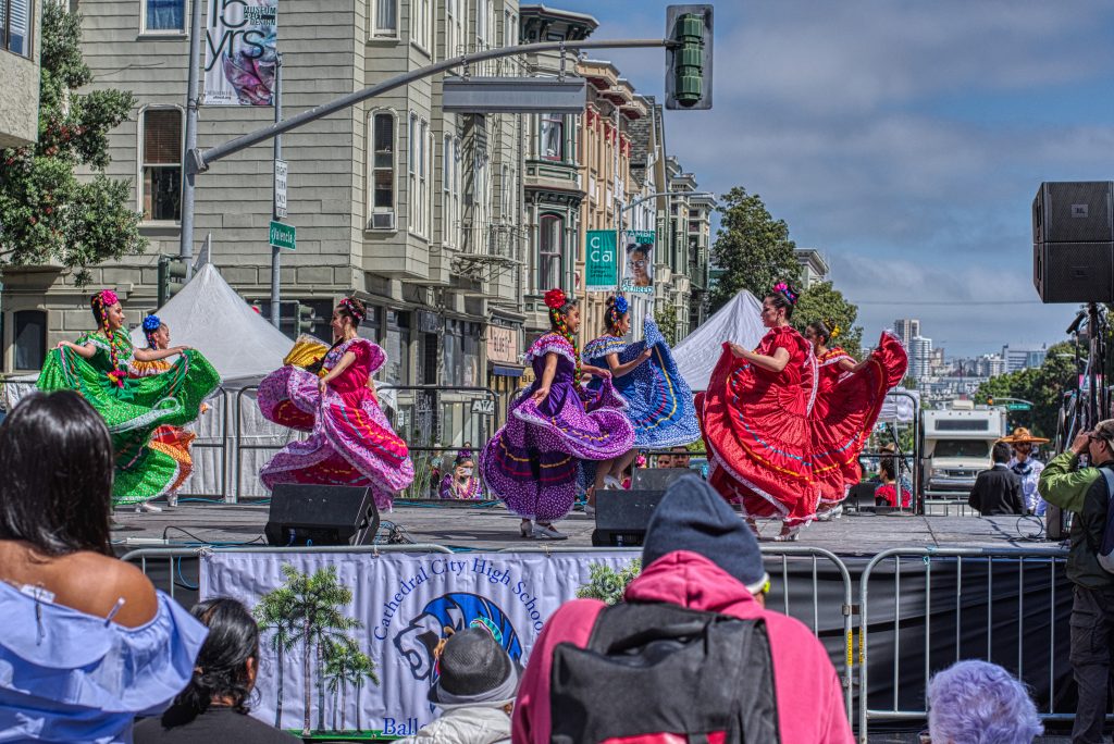 Latina women wearing traditional, colorful dresses performing on stage at San Francisco, during Cinco de Mayo celebration. 