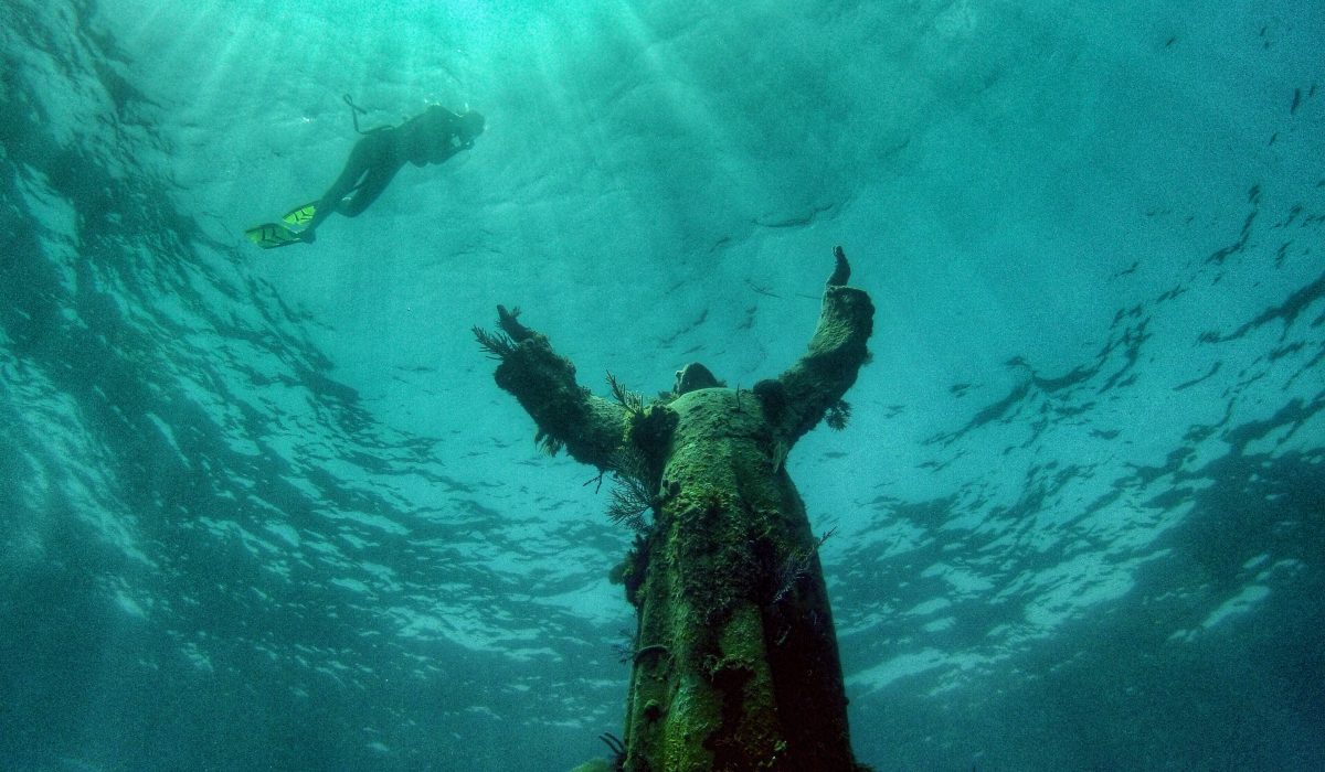 things to do in key largo Scuba diver floating near underwater Christ of the Abyss statue at Key Largo, Florida.