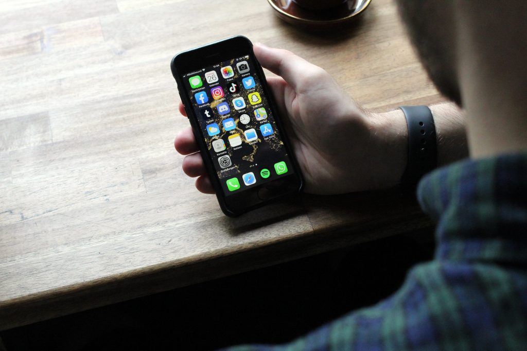 A man looking at his phone that features multiple social media platforms.