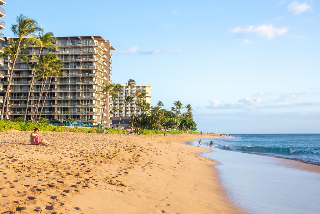 People lounging on one of the West Maui beaches with hotel buildings and palm trees in the background. People lounging on one of the West Maui beaches with hotel buildings and palm trees in the background.