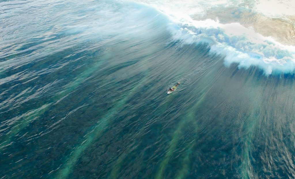 Aerial shot of a person on a surfboard with a large wave behind them in the waters of Maldives.