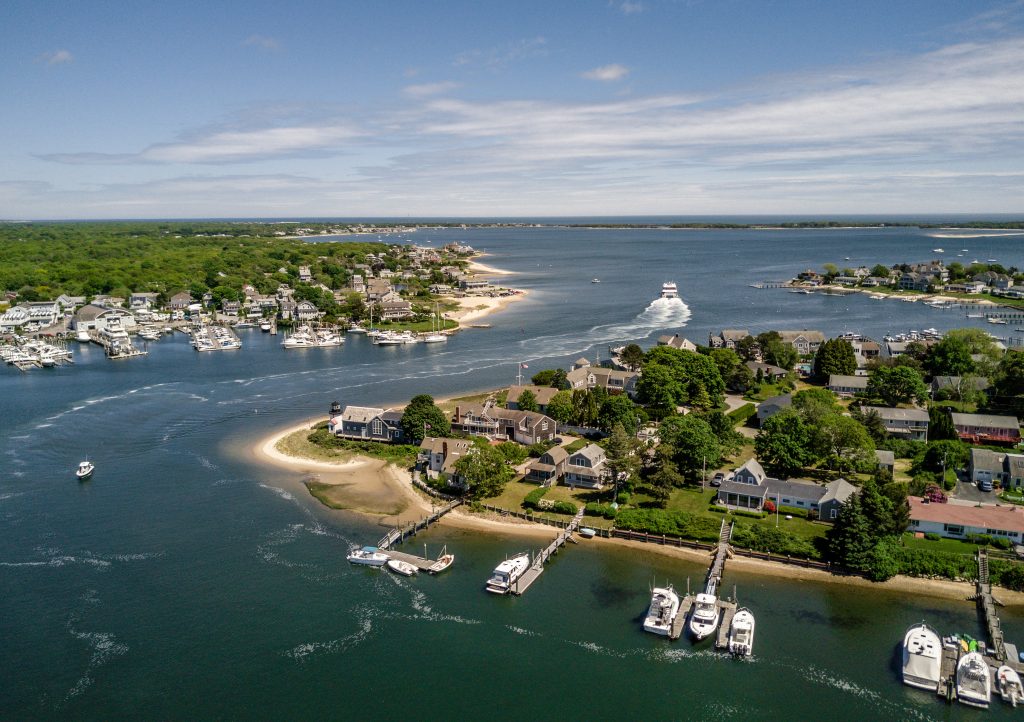 Aerial shot of the peninsula of Cape Cod with houses, greenery, and boats in the water.