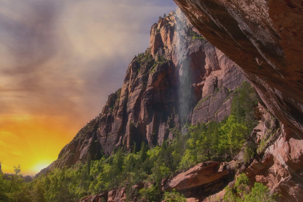 Low angle shot of water falling over the edge of a cliff in Zion National Park, Utah during sunset.